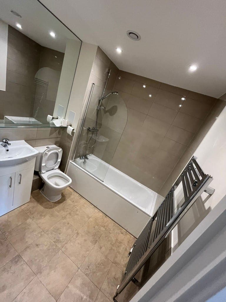 Clean end of tenancy bathroom with a white bath, glass shower screen, toilet, basin vanity unit and polished heated towel rail