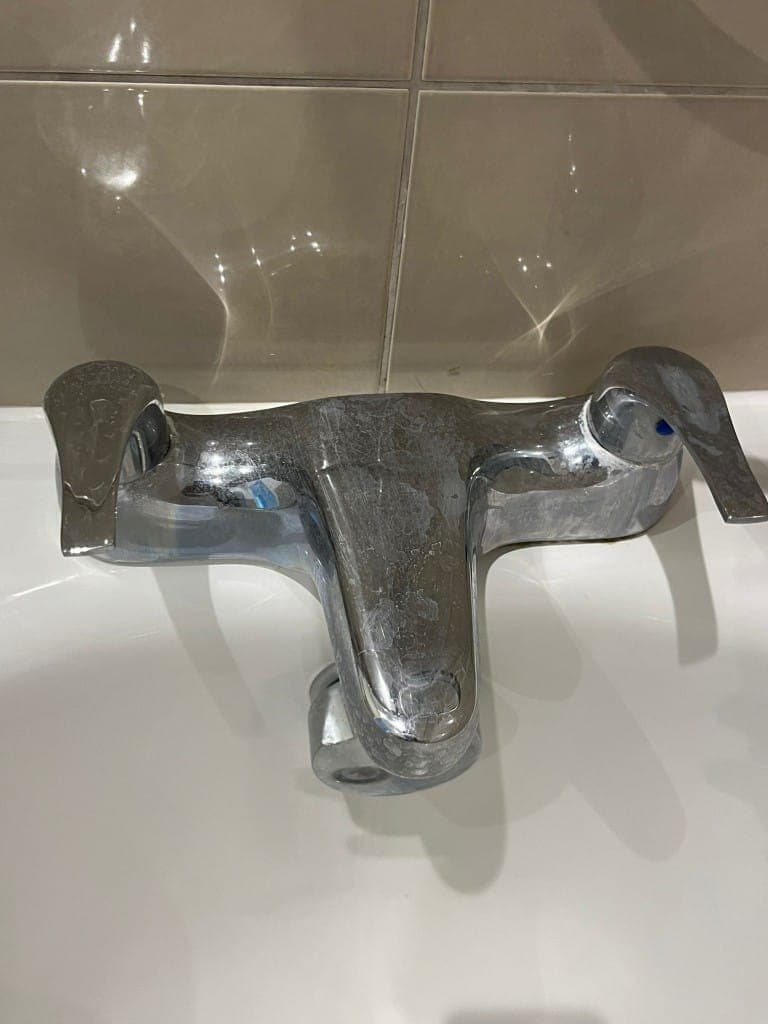 Bathroom tap before cleaning: chrome basin mixer covered in limescale, water marks and a dull cloudy finish