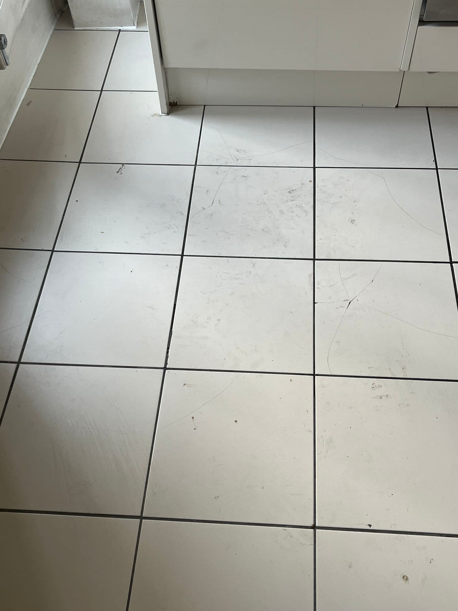 Dirty, marked white tiled kitchen floor with discoloured grout before cleaning