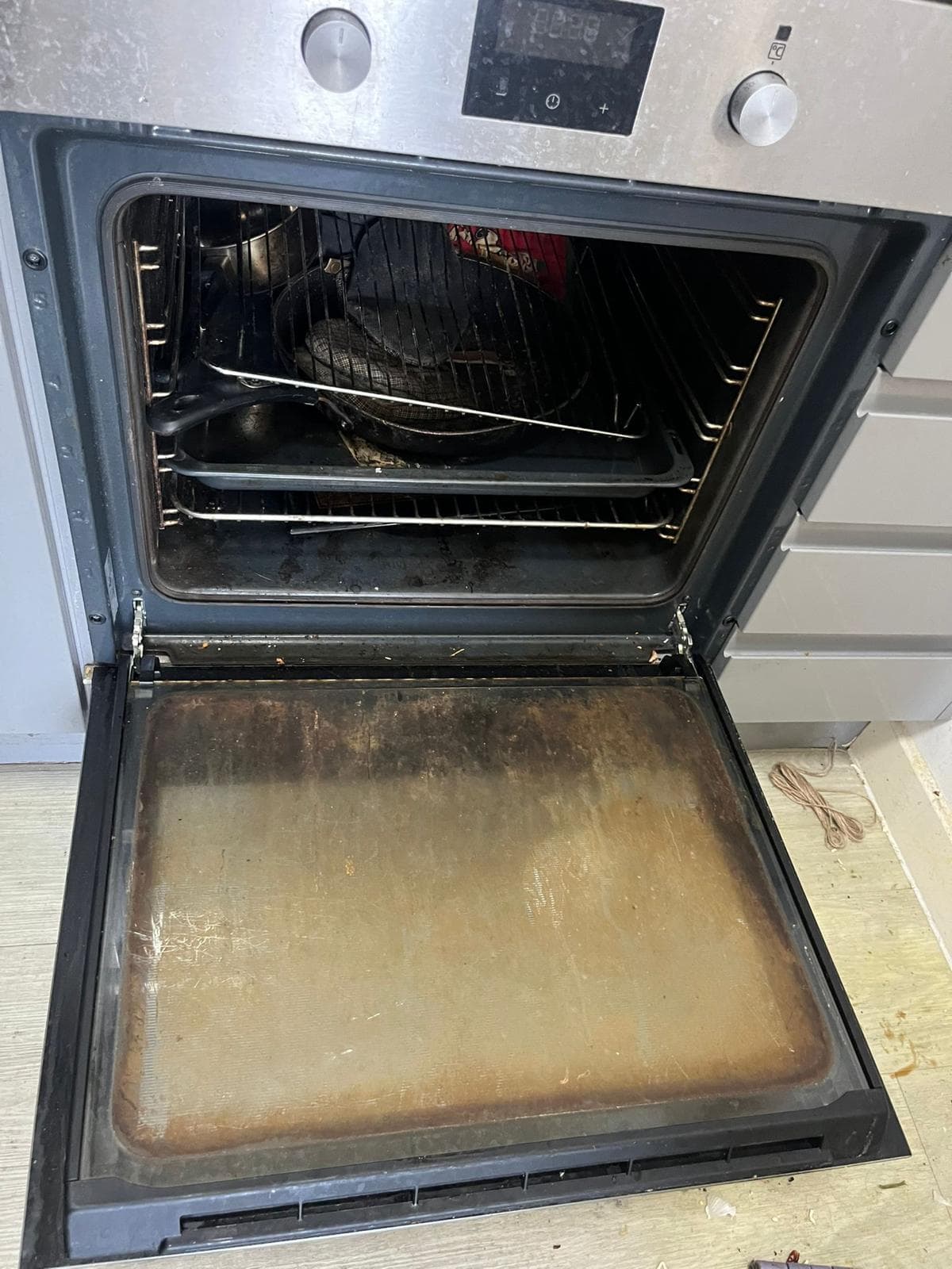 Heavily soiled oven interior with burnt-on grease, dirty racks and trays before cleaning