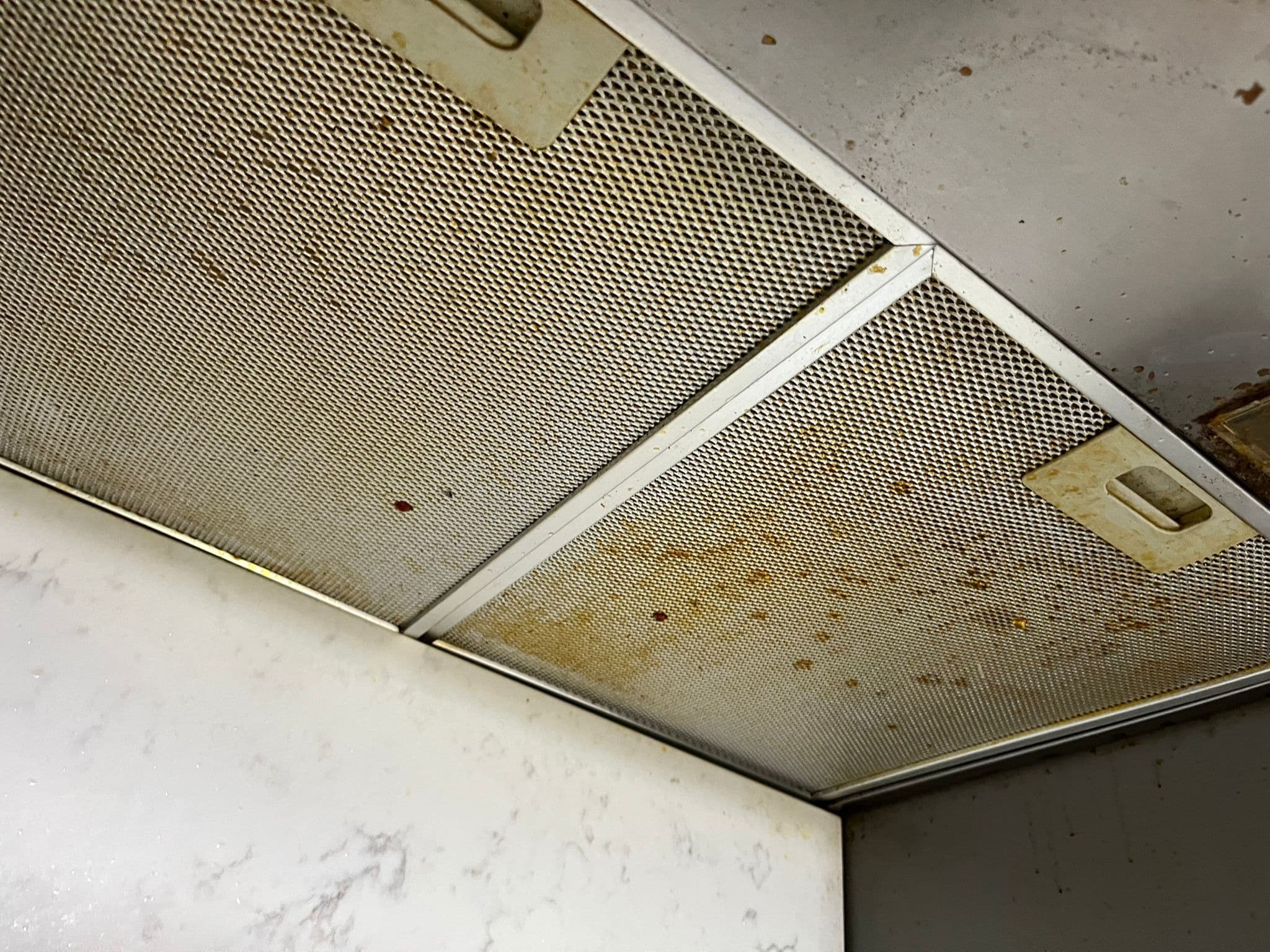 Greasy, stained metal extractor hood filters above a hob before cleaning