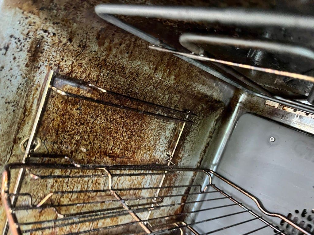 End of tenancy oven cleaning before: oven interior caked in burnt-on carbon, grease and rust-coloured staining with dirty wire racks