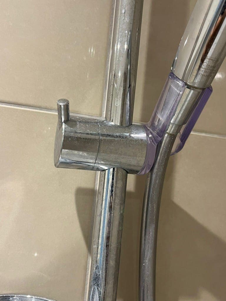 Shower rail before cleaning: chrome riser rail and bracket coated in limescale and hard-water residue